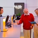 Elderly couple, one with walking stick, chat with concierge