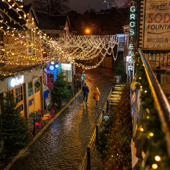 Couple walking along a cobbled street at night hung with fairy lights