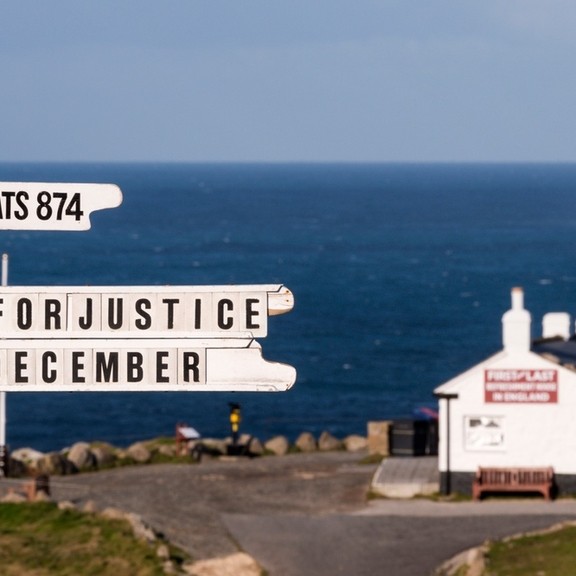 White painted signpost on a clifftop at Lands End. White building