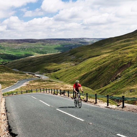 Cyclist riding on road through green dales. Panoramic views