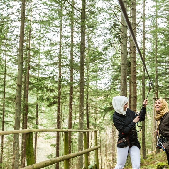 Girls standing on the zipwire platform in the pine forest