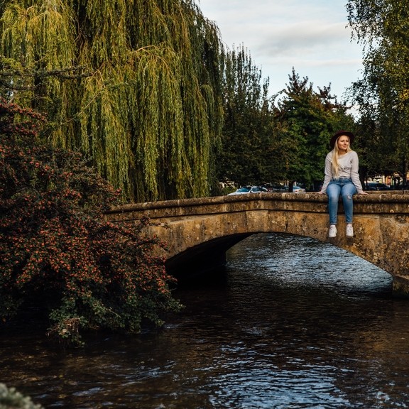 Blond woman wearing hat and jeans sitting on bridge