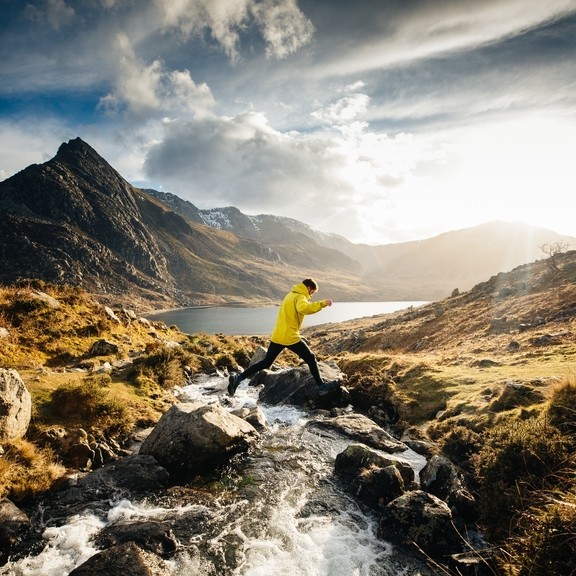 A man jumping across a stream whilst hiking