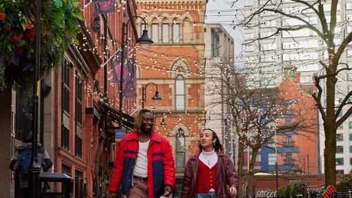 Two men walking along a shopping strip by a canal.