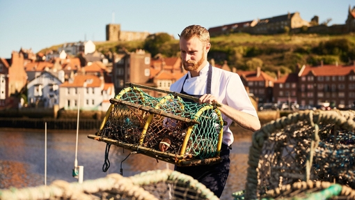 Man holding a lobster trap on a pier in the sunshine