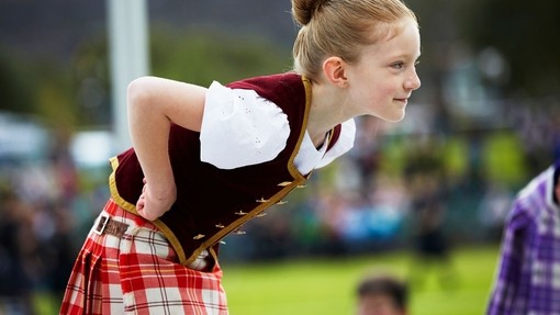 A young girl wearing a kilt leans forward while dancing