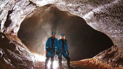 A couple standing in ankle-deep water within a back lit cave