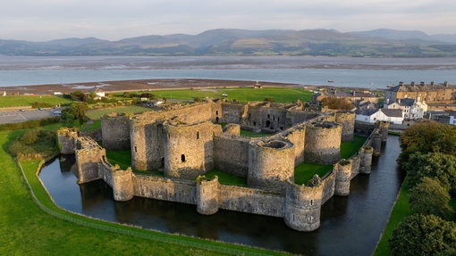 Aerial view of a large castle surrounded by water moat and hills in the background