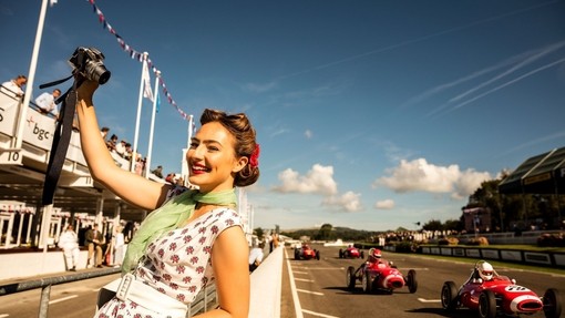 Woman taking a selfie in vintage dress standing by a car racing track