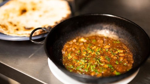 An iron skillet filled with curry and naan bread