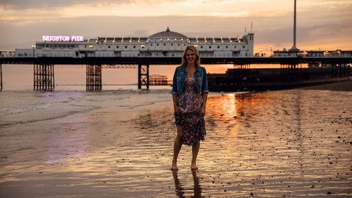 Woman standing on the beach near the pier at sunset