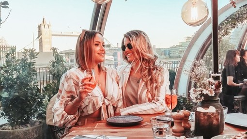 Two women enjoying food and drink in a glass dining pod on the Thames riverside