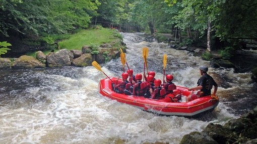 A group of children in a large dinghy with an instructor going down some what water rapids