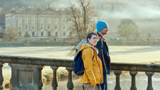 Couple walking on a stone bridge, a large country house in the backround