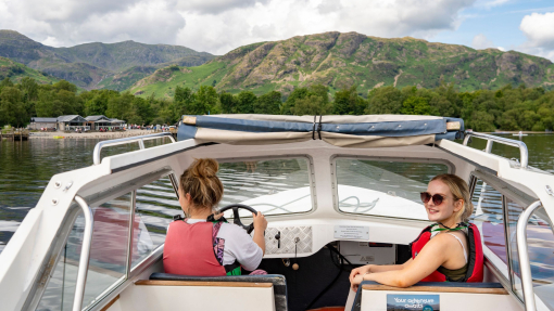 Town women sit ar the front of a boat on a lake with hills beyond