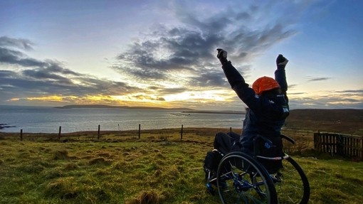 Wheelchair user, arms outstretched, watching the sunrise