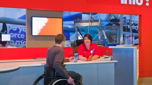 Male wheelchair user at museum talking to female staff member