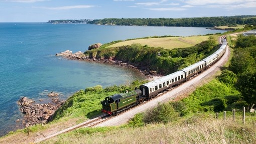 Steam train on railway line along coastline. Sea views
