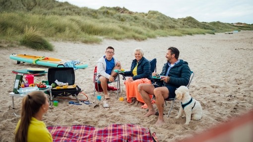A family and their dog sat beside a picnic blanket on beach
