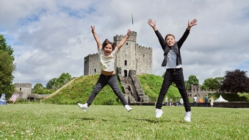 Two children jumping in front of a castle