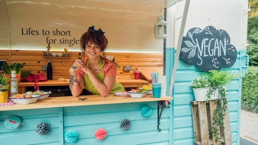 Young mixed race woman stood in the hatch of a food truck smiling, ready to serve