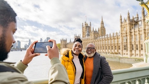A man photographing mature couple with River Thames and Houses of Parliament in background.