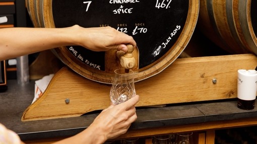 Woman's hands pouring a dram of whisky from a barrel.