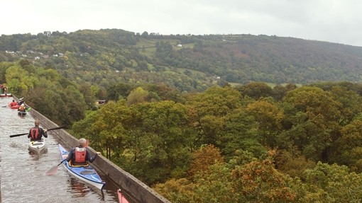 People canoeing across an elevated aqueduct with views of the valley below.