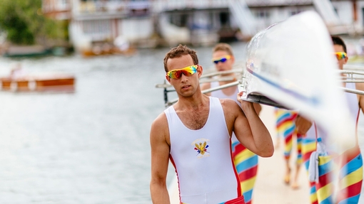 Rowers carrying a racing scull by the side of a river