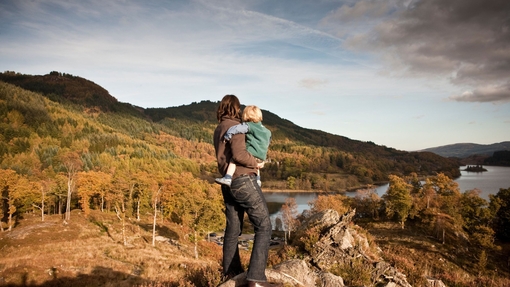 Woman and child standing on a hilltop overlooking a lake.