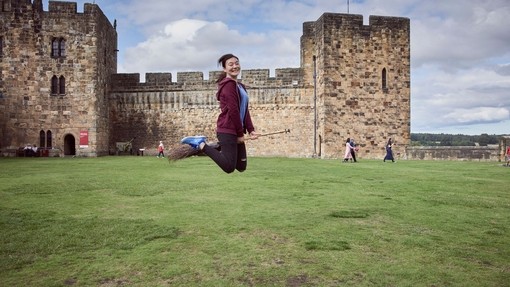Young woman hovering on a broomstick in the Outer Bailey of Alnwick Castle