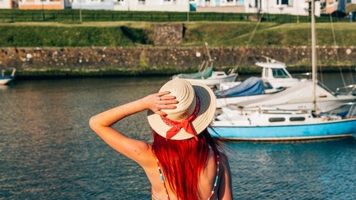 Woman sitting on the wall of a harbour looking at the boats