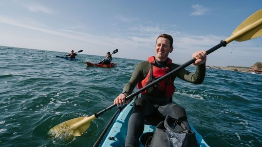 A man kayaking with two other people kayaking in the background.
