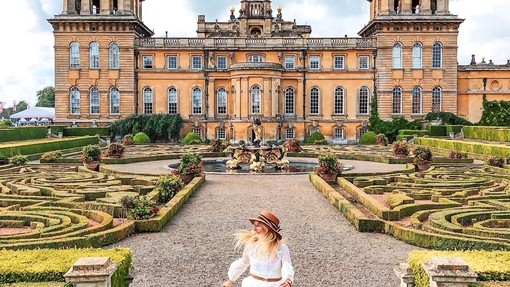 Woman walking in Blenheim Palace gardens surrounded by greenery and manicured topiary.