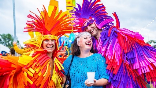 Three people hugging and smiling dressed in colourful costumes at a festival