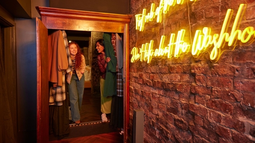 Two women laughing, exploring the cupboard entrance of a trendy city bar.