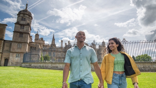 A man and woman holding hands and walking in front of a heritage building