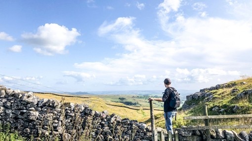 Man standing on stile over stone wall looking at landscape