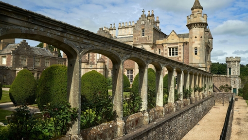 Large stately home and manicured gardens as seen through a stone arch wall