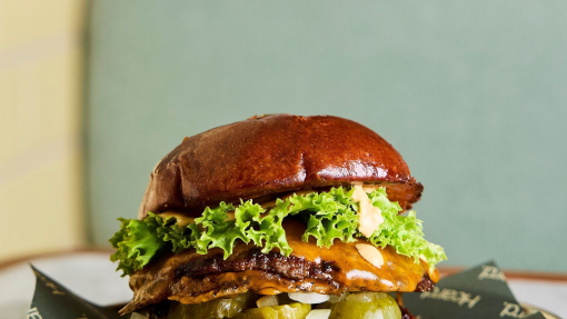 A burger stacked with meat, cheese, pickles and lettuce on a plate, on a marble table.