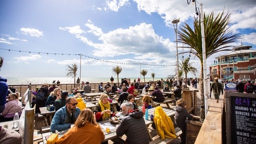 People enjoying drinks and food outside on Brighton sea front at Fortune of War bar in Brighton.
