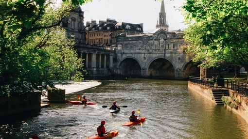 Group of people kayaking on the river in the sunshine by Pulteney Bridge, Bath