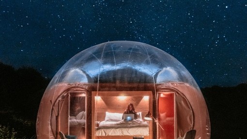 Large glamping bubble pod lit up with woman inside