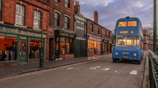 A vintage blue bus driving down a street in a living museum