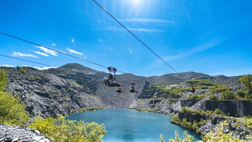 People on a high zip wire going over a quarry filled with water.