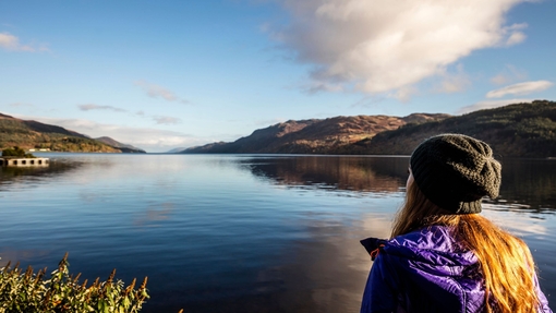 Woman standing on the shores of a lake surrounded by hills