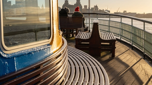 View from on board a ferry looking towards the city skyline with a Union Jack flag and two passengers on board