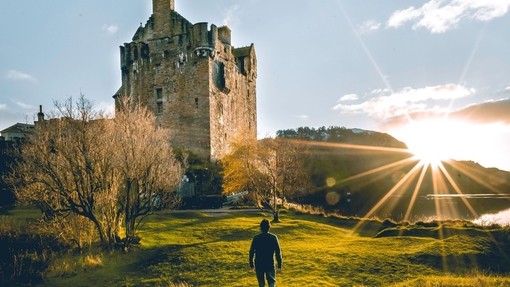 Man walking towards a castle with sun rising in the sky
