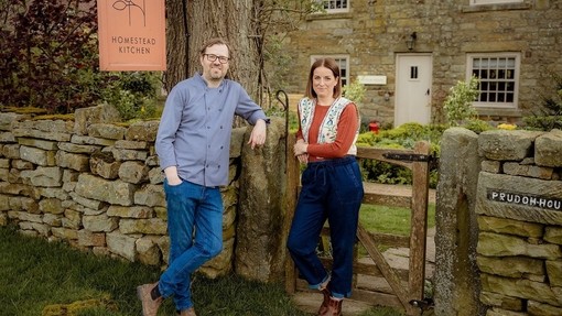 Two people standing in front of a countryside cottage. A sign reads: Homestead Kitchen