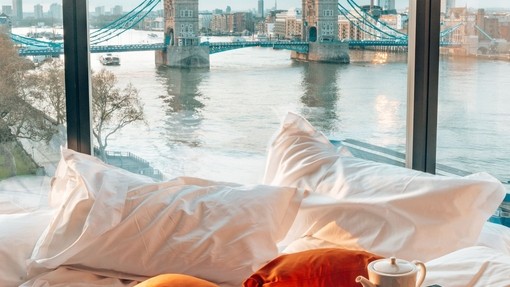 An unmade bed with views of Tower Bridge from window
